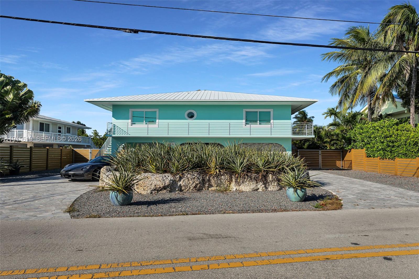 A light blue two-story house features a balcony, a rock garden, and a paved driveway — 232 W Seaview Dr, Duck FL 33050, DUCK, FL
