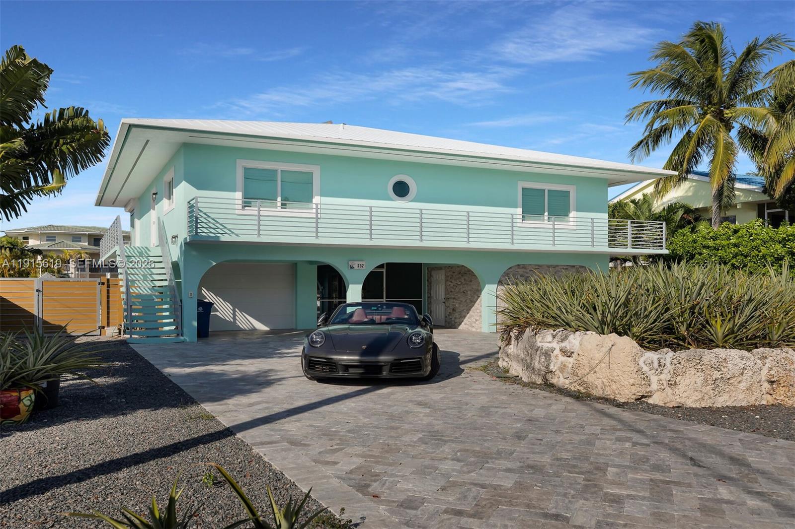 A two-story light blue house with a balcony and a car parked in the driveway — 232 W Seaview Dr, Duck FL 33050, DUCK, FL