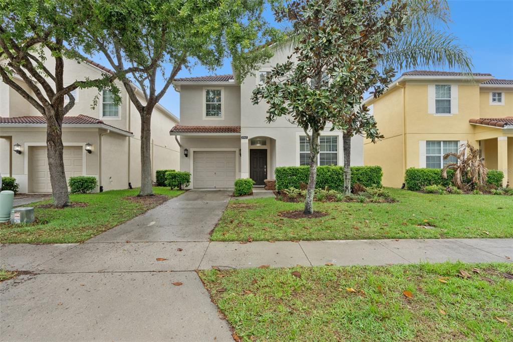 A two-story suburban house with a beige stucco exterior, a single-car garage, and front landscaping — 8965 CUBAN PALM ROAD, KISSIMMEE, FL
