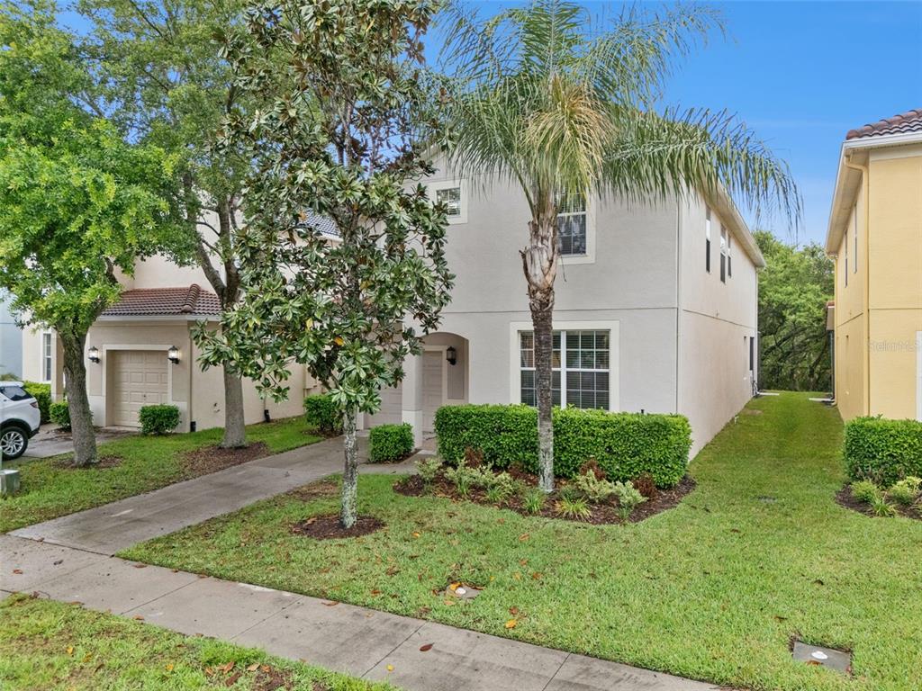 A two-story light-colored house with a palm tree, manicured hedges, and a concrete driveway — 8965 CUBAN PALM ROAD, KISSIMMEE, FL