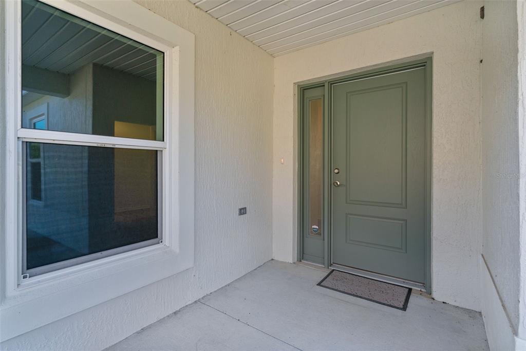 A covered entryway features a sage green front door with a side window and stucco walls — 1363 DARREN DRIVE, THE VILLAGES, FL