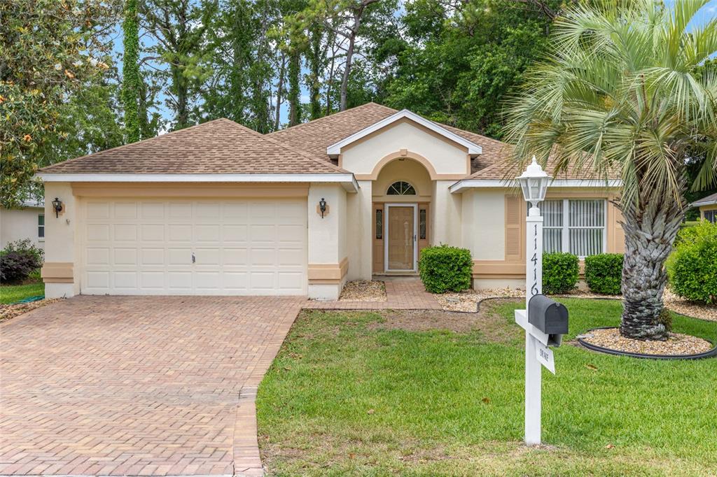 A single-story house with a beige stucco exterior, a brick driveway, and a palm tree — 11416 SW 69TH CIR, OCALA, FL
