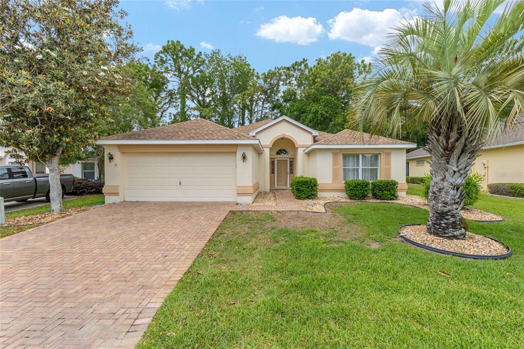 A single-story house with a beige stucco exterior, a brick driveway, and a palm tree — 11416 SW 69TH CIR, OCALA, FL