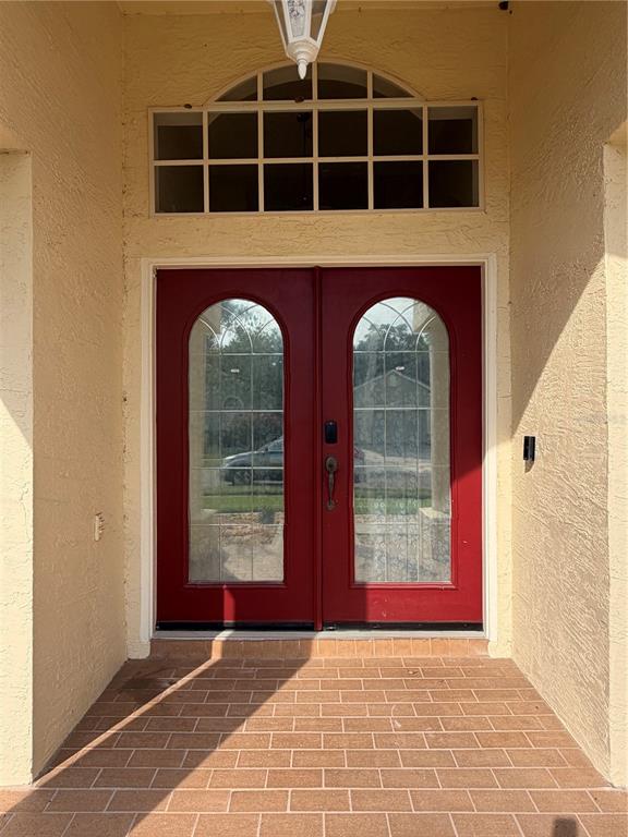 A red double front door with glass inserts sits beneath an arched transom window — 731 FORESTGREEN COURT, ORLANDO, FL
