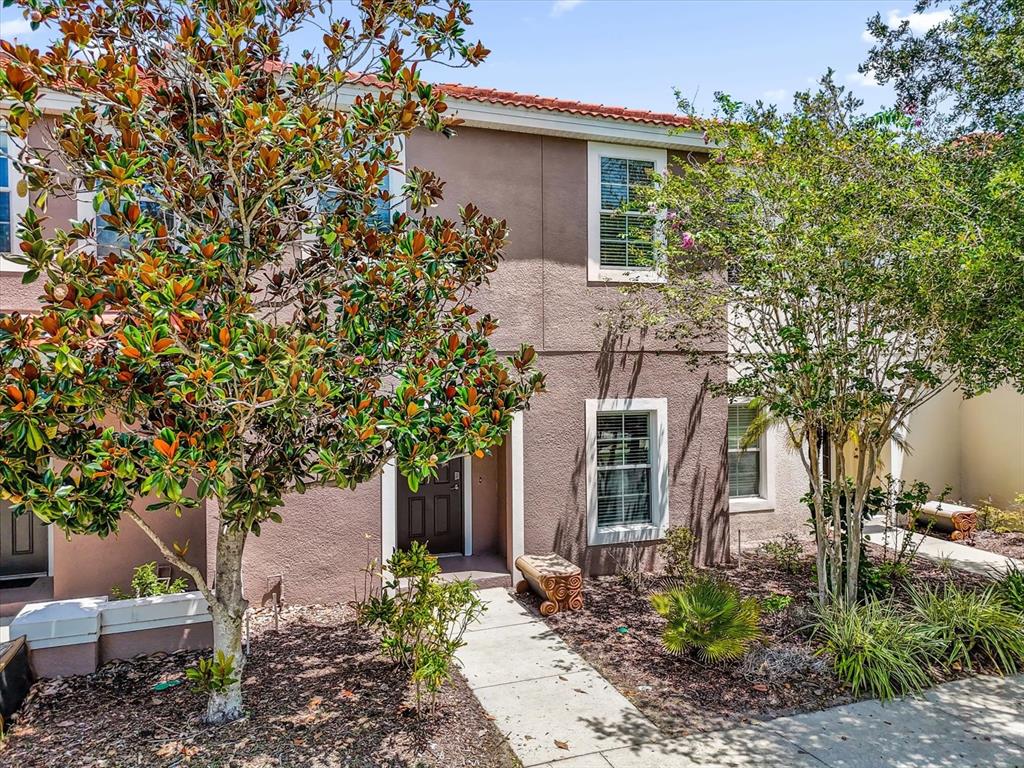 A two-story tan stucco townhouse with a tile roof, front entrance, and landscaped yard — 4569 CORSA LANE, KISSIMMEE, FL