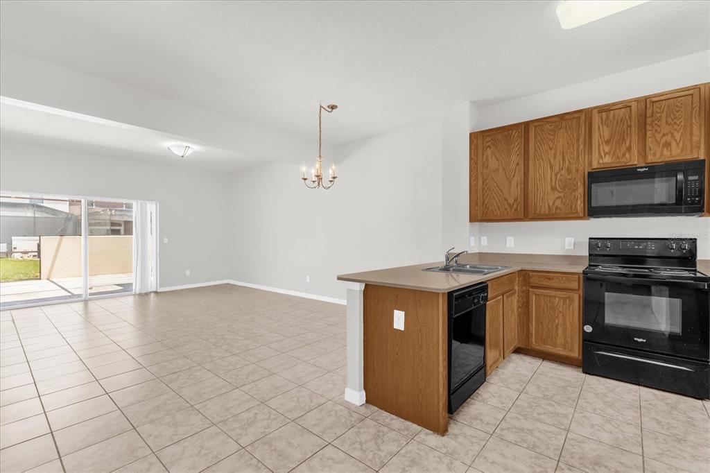 A kitchen with wood cabinets and black appliances overlooks an open living area with tile — 4569 CORSA LANE, KISSIMMEE, FL