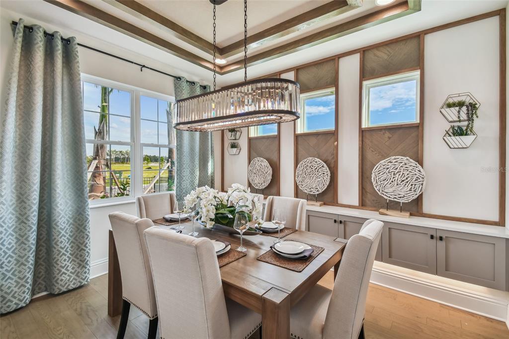A dining room features a wooden table, upholstered chairs, a crystal chandelier, and paneled walls — 5950 NEWBERRY PINES AVENUE, WESLEY CHAPEL, FL
