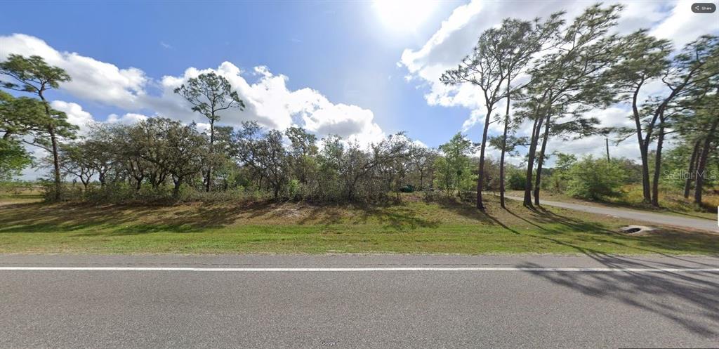 A grassy, wooded vacant lot sits alongside a paved road under a partly cloudy sky — COMMONWEALTH AVENUE N, POLK CITY, FL