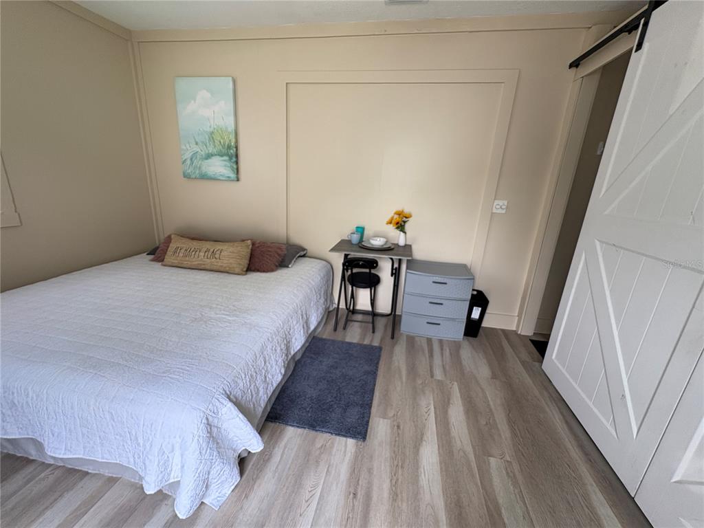 A bedroom features light wood-look flooring, a bed with a white quilt, and a small desk — 14413-B HERTHA AVENUE, ORLANDO, FL