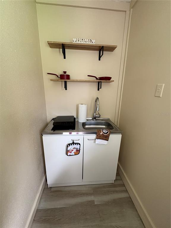 A small kitchenette features a stainless steel sink, a portable cooktop, and two wooden shelves — 14413-B HERTHA AVENUE, ORLANDO, FL