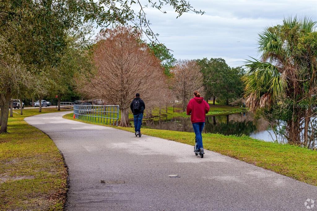 Two people ride electric scooters along a paved path beside a pond and trees — 14413-B HERTHA AVENUE, ORLANDO, FL
