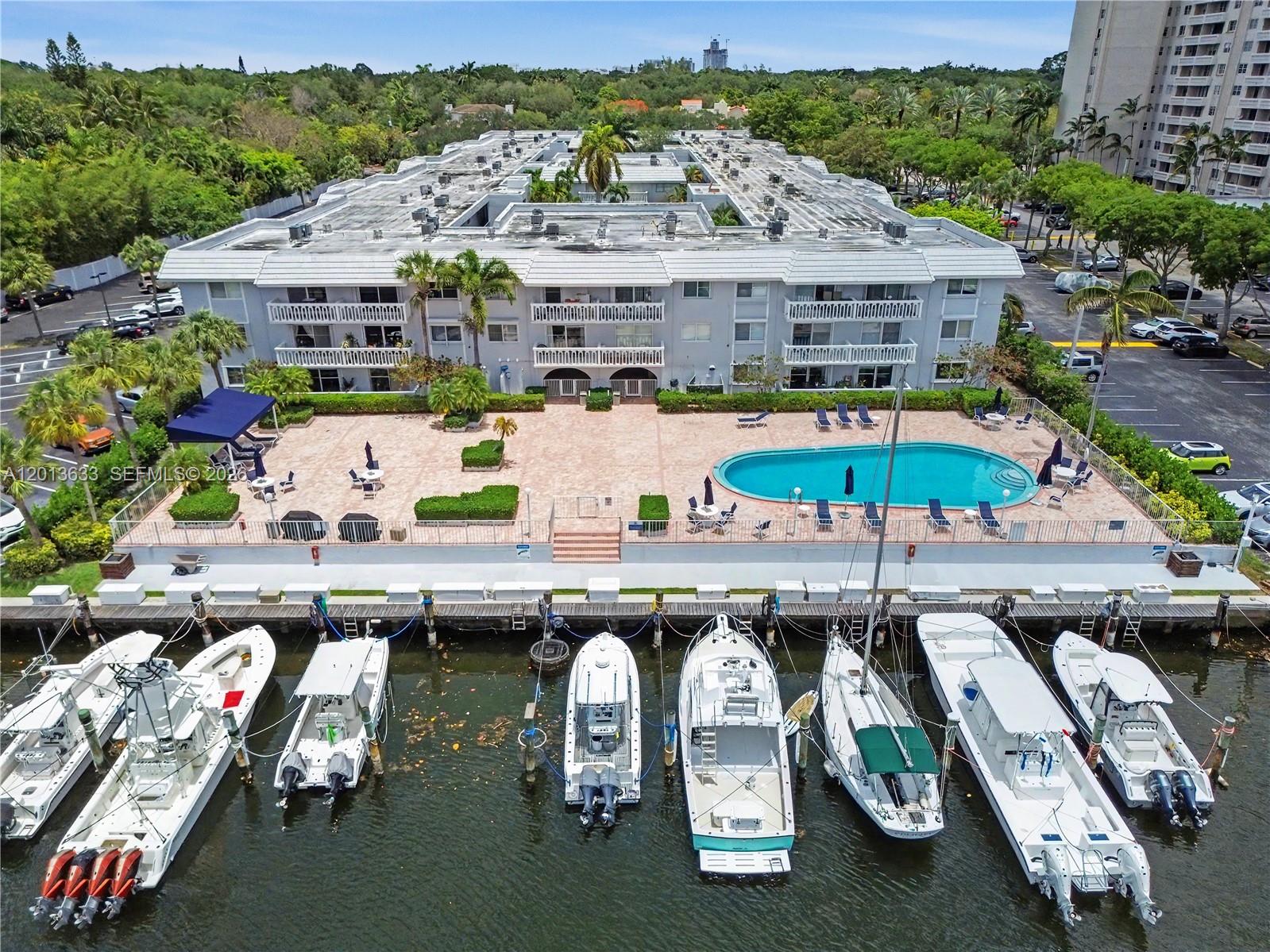 An aerial view shows a multi-story apartment building with a pool deck and boat slips — 100 Edgewater Dr # 204, Coral Gables FL 33133, CORAL GABLES, FL