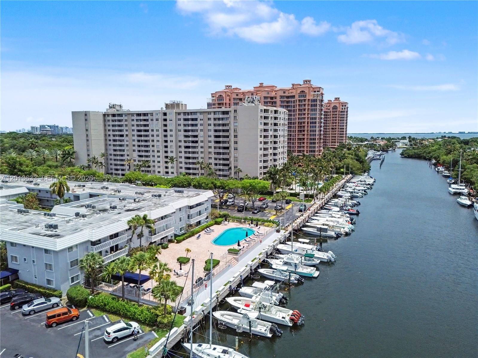 An aerial view shows a residential complex with a swimming pool and a boat-lined canal — 100 Edgewater Dr # 204, Coral Gables FL 33133, CORAL GABLES, FL