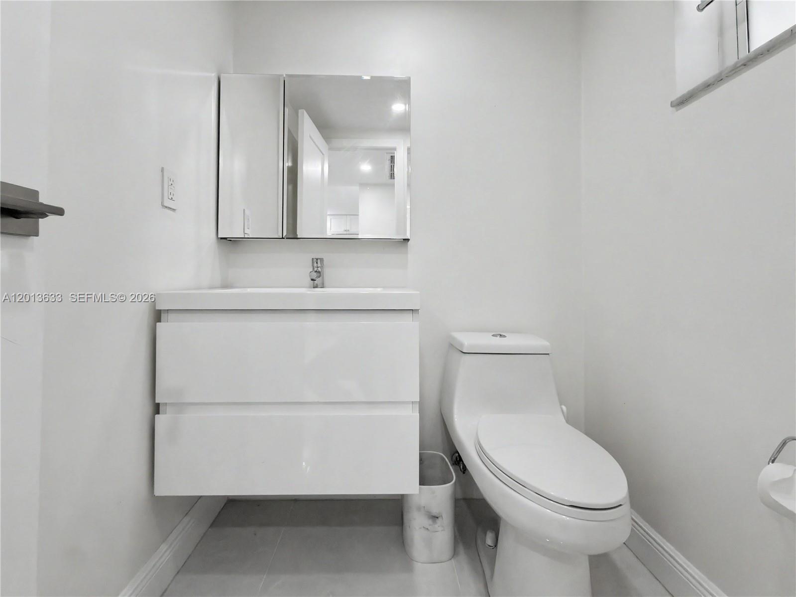 A modern bathroom features a white floating vanity, a wall-mounted mirror, and a white toilet — 100 Edgewater Dr # 204, Coral Gables FL 33133, CORAL GABLES, FL