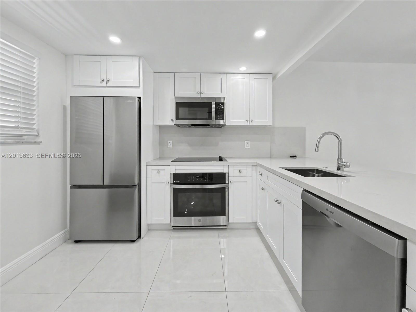 A modern kitchen features white cabinets, stainless steel appliances, and light-colored tile flooring — 100 Edgewater Dr # 204, Coral Gables FL 33133, CORAL GABLES, FL