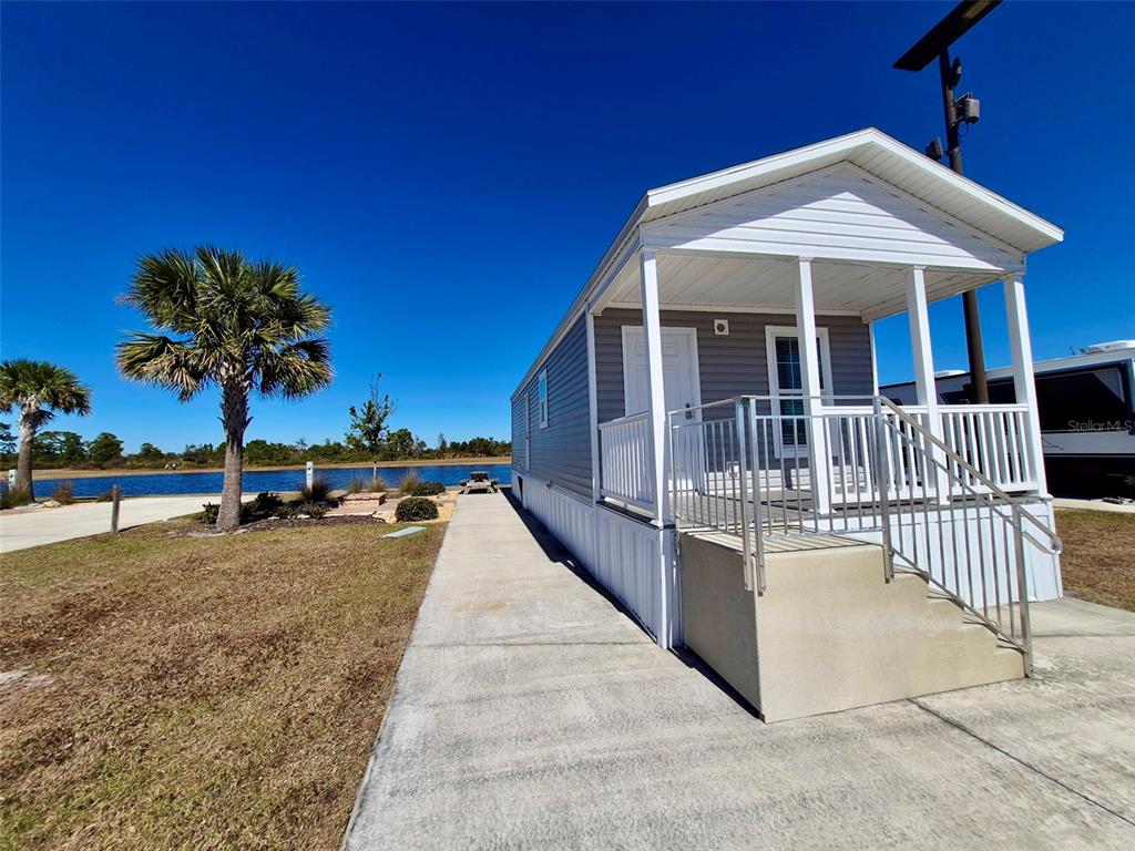 A gray mobile home with a front porch sits on a concrete pad near water — 0 HIGHWAY 630 E UNIT 74, LAKE WALES, FL