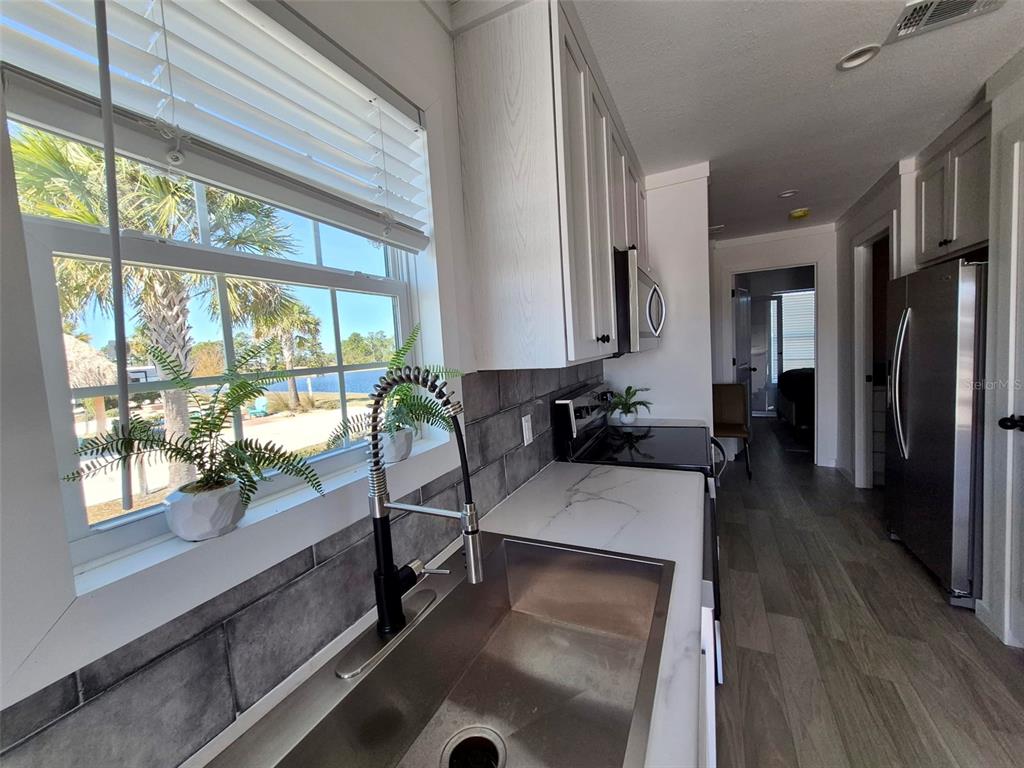 A kitchen features a stainless steel sink, white cabinets, dark tile backsplash, and a window view — 0 HIGHWAY 630 E UNIT 74, LAKE WALES, FL