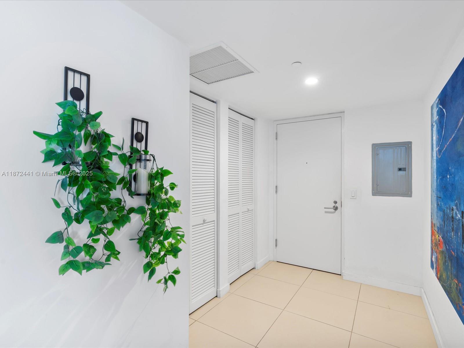 An entryway features white walls, tiled floors, louvered closet doors, and wall-mounted artificial plants — 31 SE 6th St # 802, Miami FL 33131, MIAMI, FL
