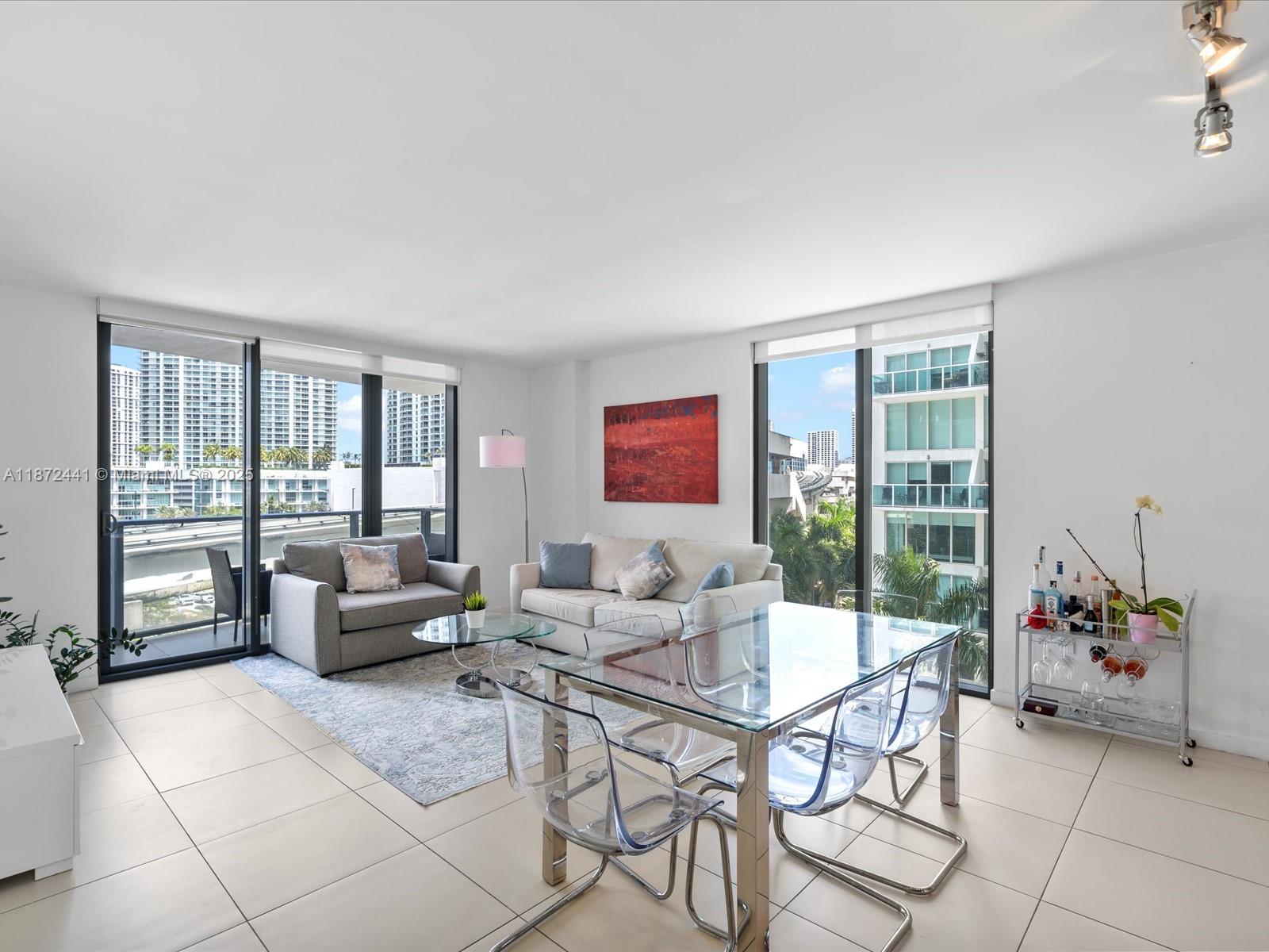 A bright living and dining area features tile floors, glass furniture, and floor-to-ceiling windows — 31 SE 6th St # 802, Miami FL 33131, MIAMI, FL