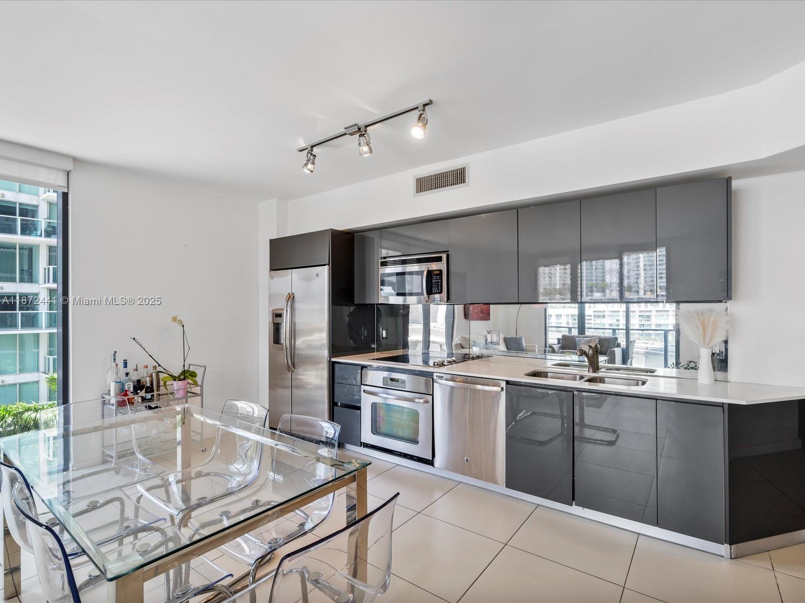 A modern kitchen features gray glossy cabinets, stainless steel appliances, and a glass dining table — 31 SE 6th St # 802, Miami FL 33131, MIAMI, FL