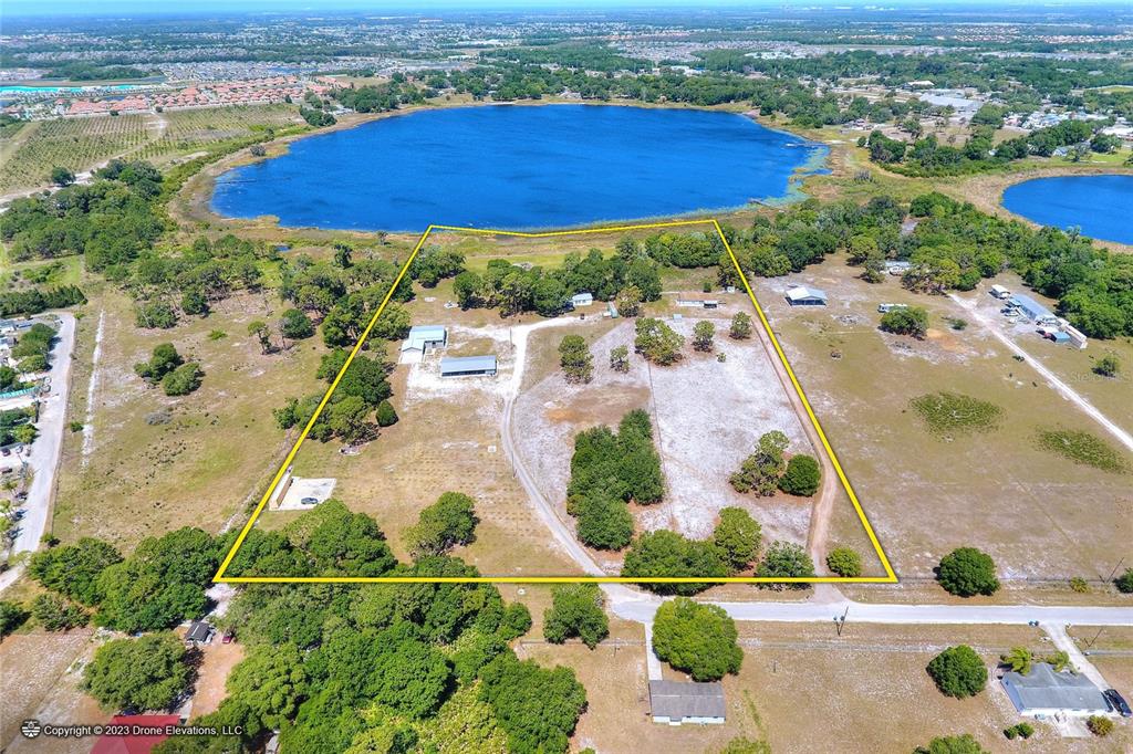 An aerial view shows a large, fenced-in grassy lot with several structures bordering a lake — 5514 HILLSBOROUGH STREET, WIMAUMA, FL