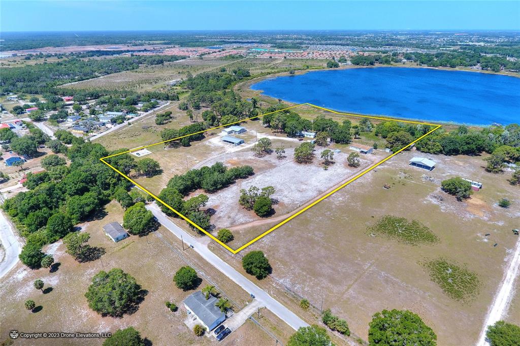 An aerial view shows a large, fenced-in rural property with several buildings near a lake — 5514 HILLSBOROUGH STREET, WIMAUMA, FL