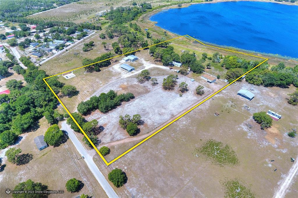 An aerial view shows a large, grassy property with several buildings bordering a lake — 5514 HILLSBOROUGH STREET, WIMAUMA, FL