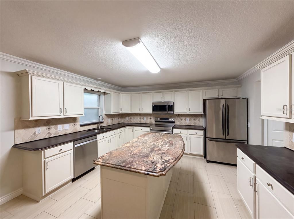 A kitchen features white cabinets, dark countertops, a stone-topped island, and stainless steel appliances — 3312 WHITE BLOSSOM LANE, CLERMONT, FL