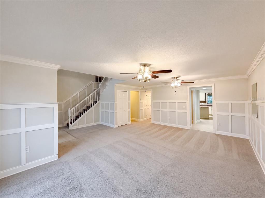 A spacious living room features carpeted flooring, white wainscoting, a staircase, and two ceiling fans — 3312 WHITE BLOSSOM LANE, CLERMONT, FL