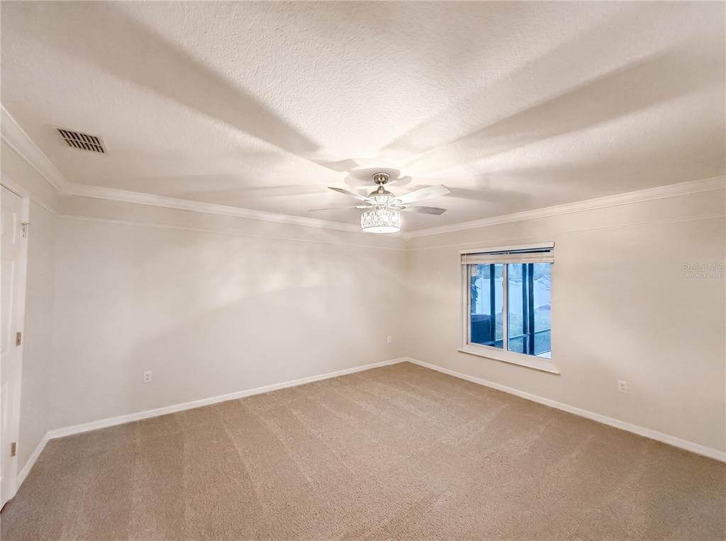 An empty bedroom features beige carpeting, white walls, crown molding, and a ceiling fan — 3312 WHITE BLOSSOM LANE, CLERMONT, FL