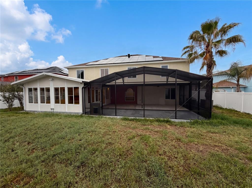 The rear exterior of a two-story house features a sunroom, a screened-in patio, and solar panels — 3312 WHITE BLOSSOM LANE, CLERMONT, FL
