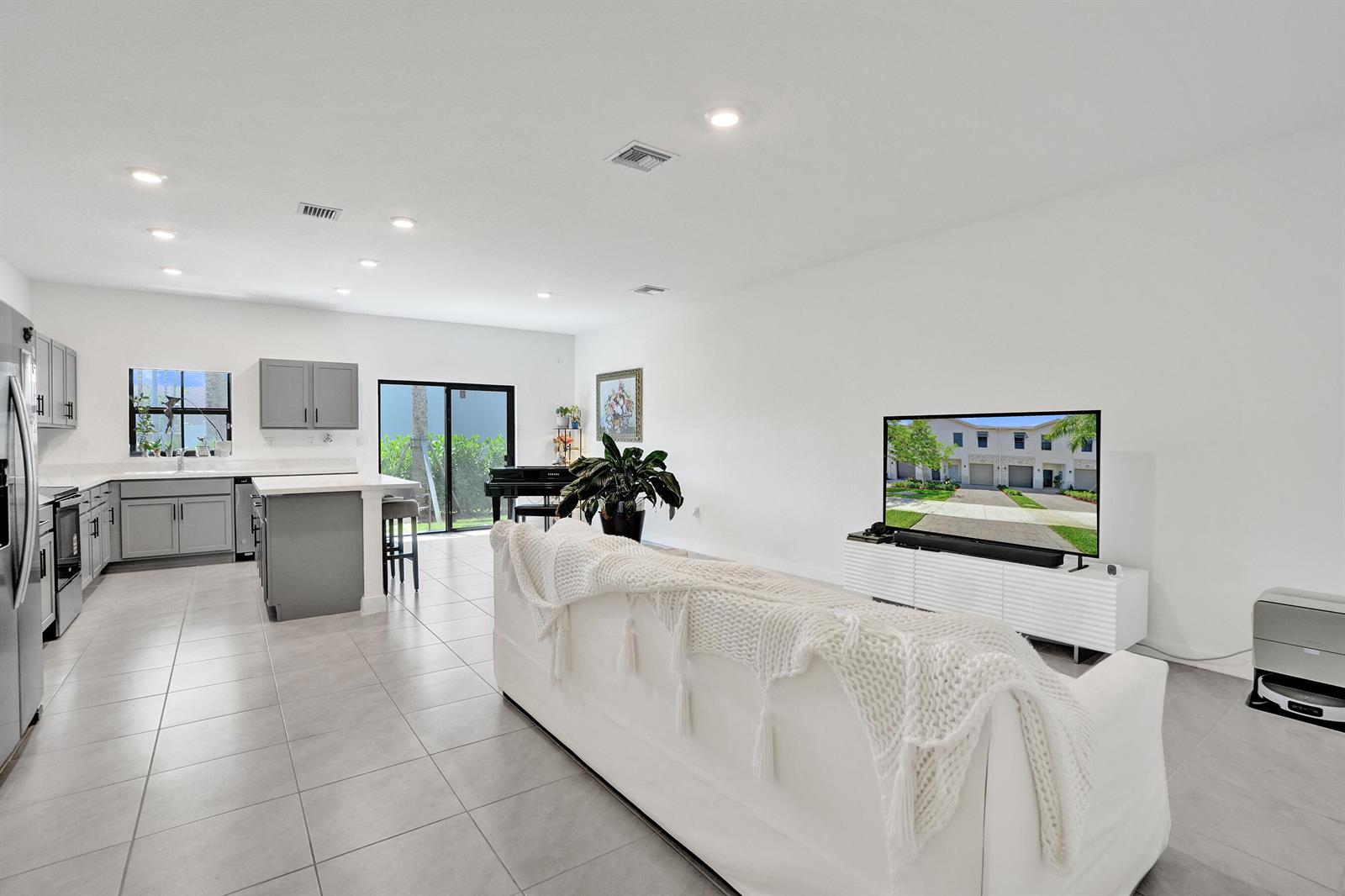A white sofa faces a television in an open-concept living room with a gray kitchen — 975 NW 3rd Terrace, Pompano Beach FL 33060, POMPANO BEACH, FL