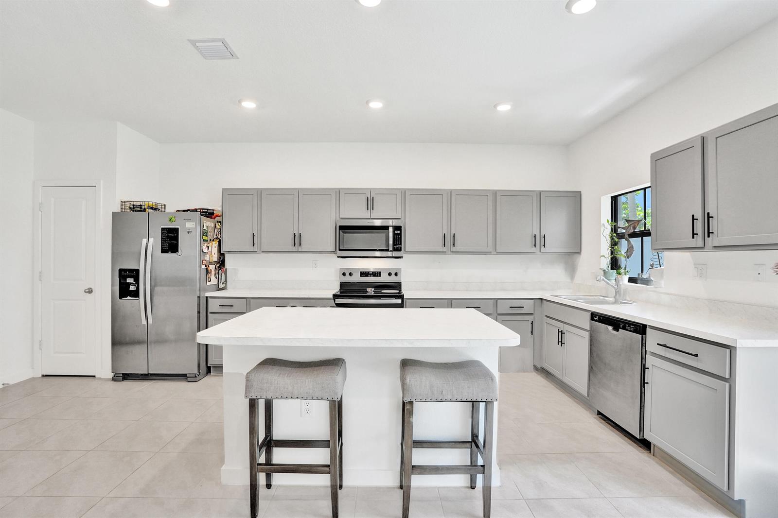 A kitchen features gray cabinets, stainless steel appliances, a white island, and light tile flooring — 975 NW 3rd Terrace, Pompano Beach FL 33060, POMPANO BEACH, FL