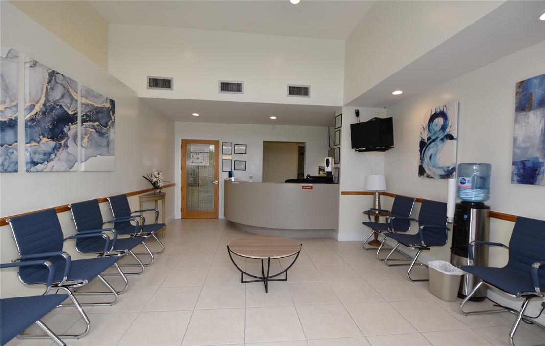 A waiting room with blue chairs, a reception desk, and abstract wall art — 1820 E Commercial Boulevard, Fort Lauderdale FL 33308, FORT LAUDERDALE, FL