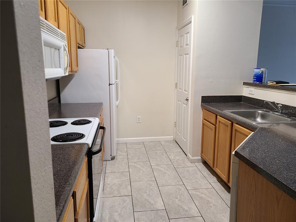 A kitchen features light wood cabinets, dark countertops, white appliances, and light gray tile flooring — 4802 51ST STREET W UNIT 602, BRADENTON, FL