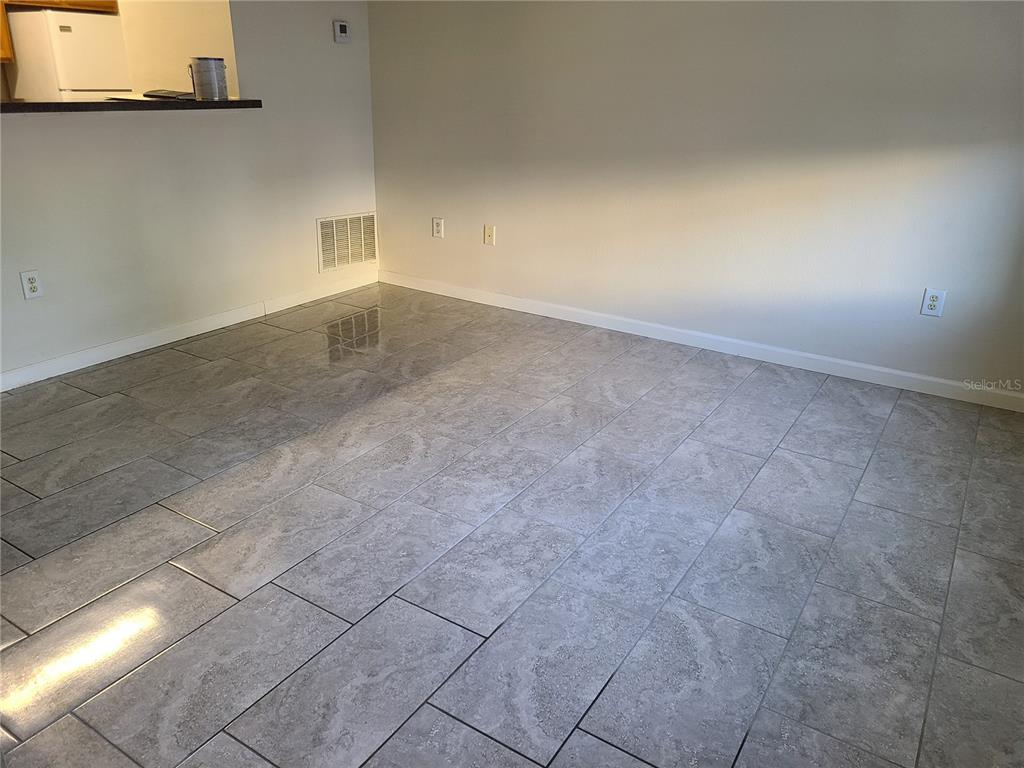 An empty room features gray tiled flooring, white walls, and a kitchen pass-through counter — 4802 51ST STREET W UNIT 602, BRADENTON, FL