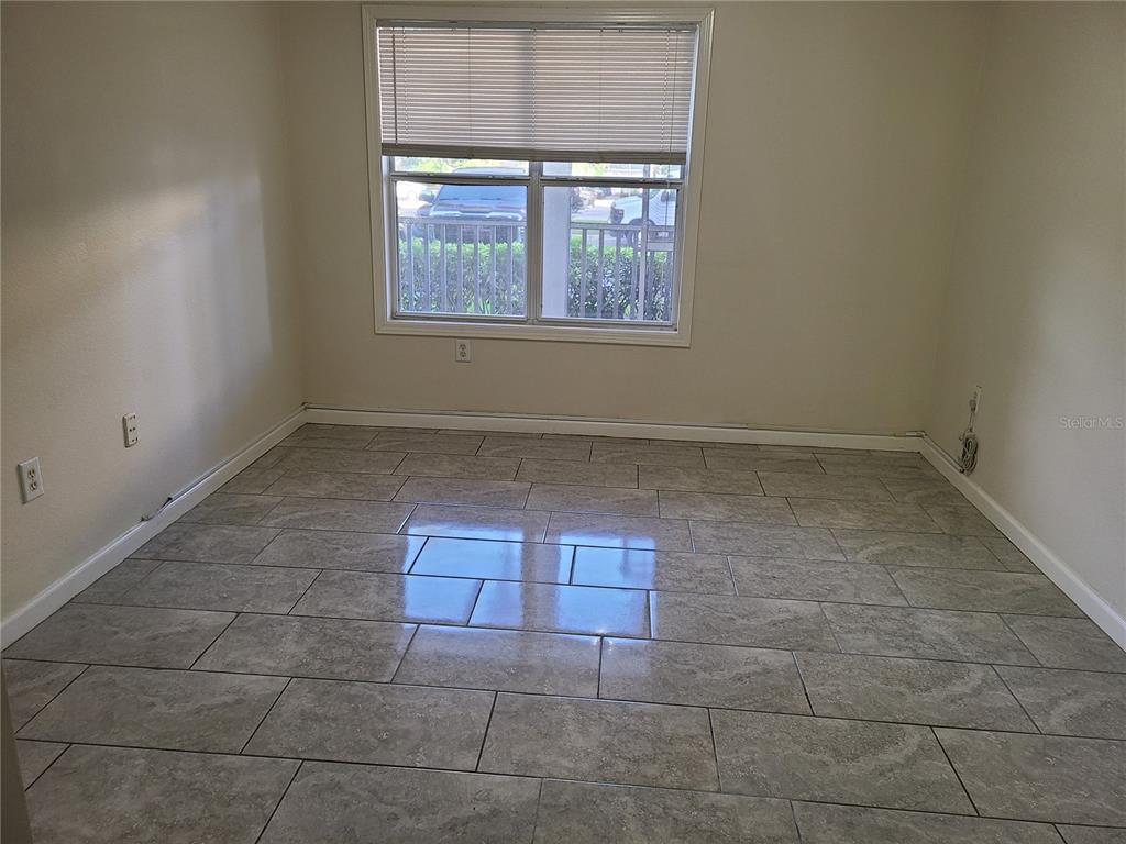 An empty room features light-colored walls, a window with blinds, and gray tile flooring — 4802 51ST STREET W UNIT 602, BRADENTON, FL
