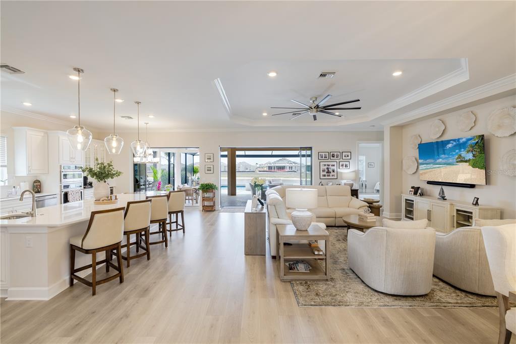 An open-concept living room and kitchen featuring light wood floors, white cabinetry, and pool views — 17602 TERRACINA DRIVE, FORT MYERS, FL