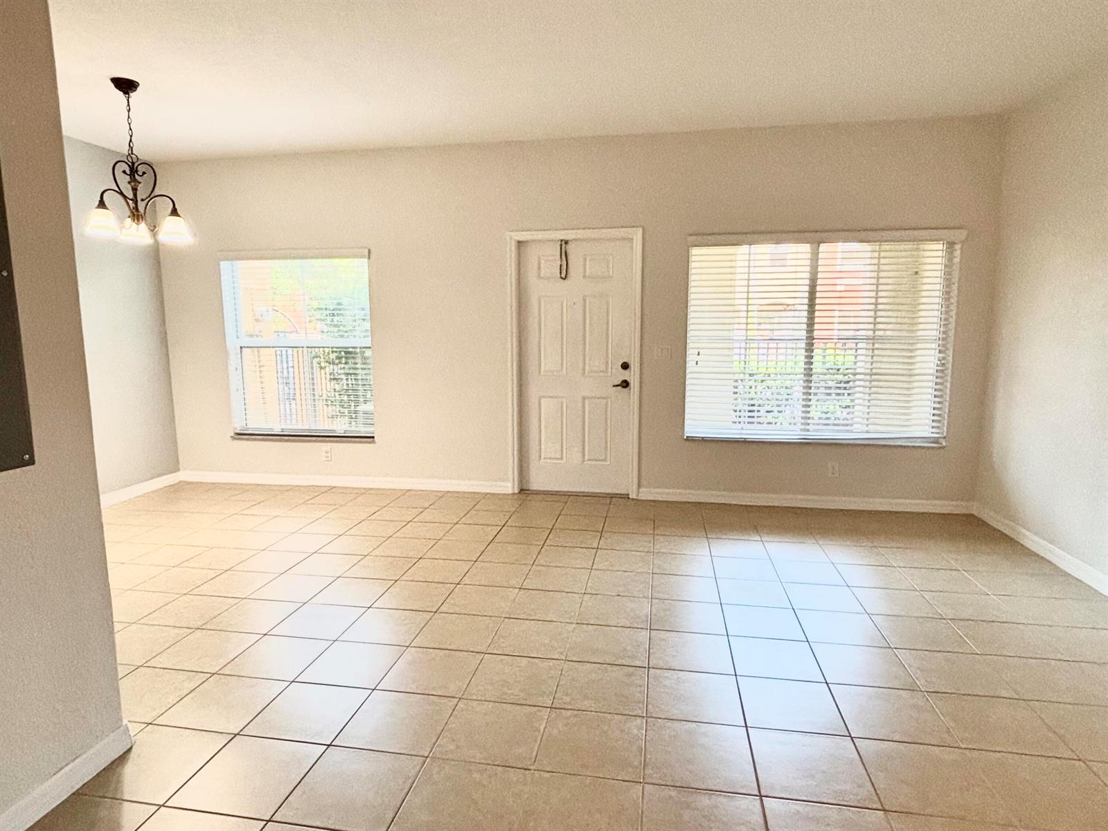 An empty room features beige tile flooring, a white front door, and two windows — 161 Monterey Bay Drive, Boynton Beach FL 33426, BOYNTON BEACH, FL