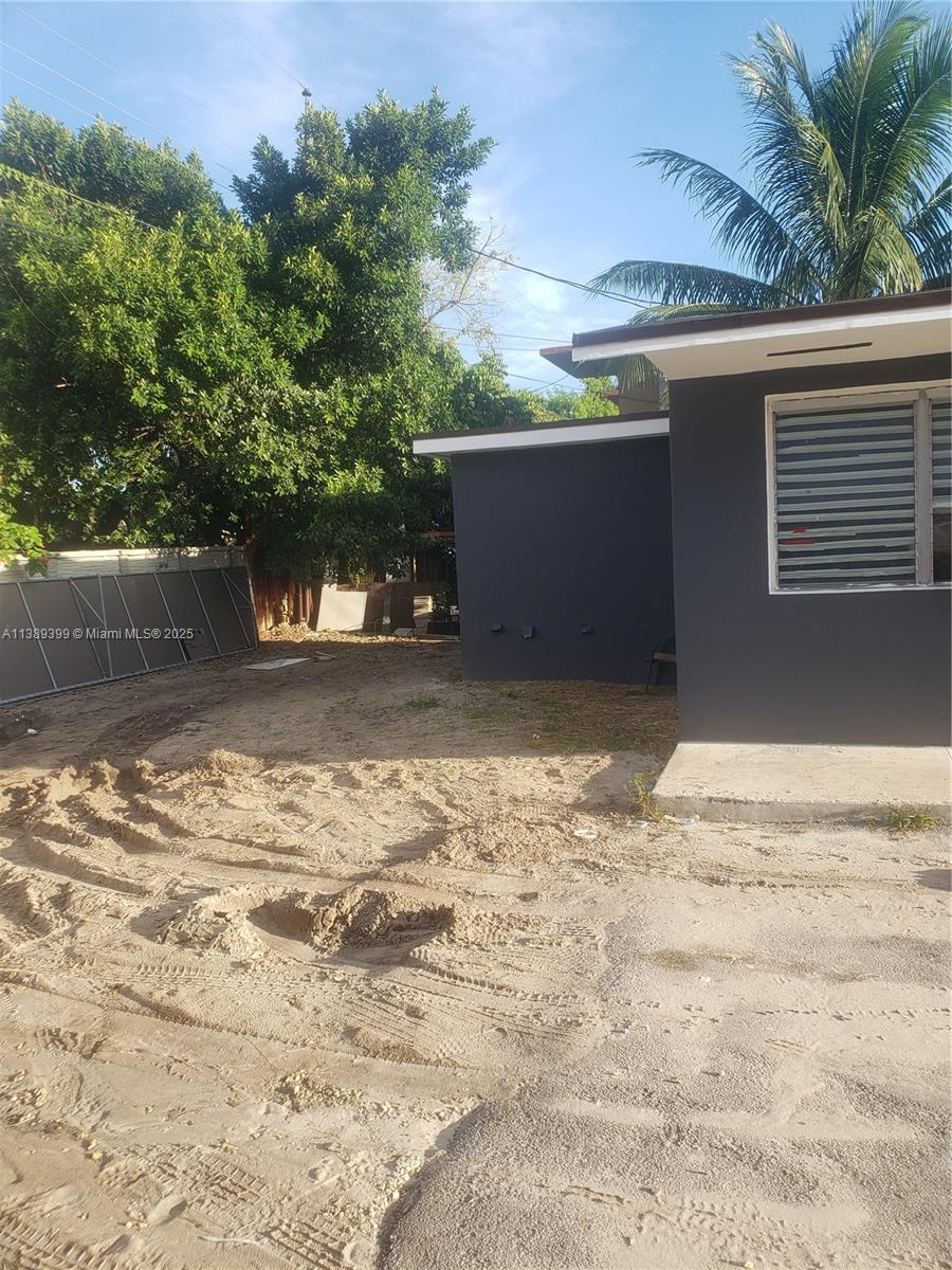 An exterior view shows a dark-painted house with a sandy, unpaved yard and large trees — 2855 NW 22nd Ave, Miami FL 33142, MIAMI, FL