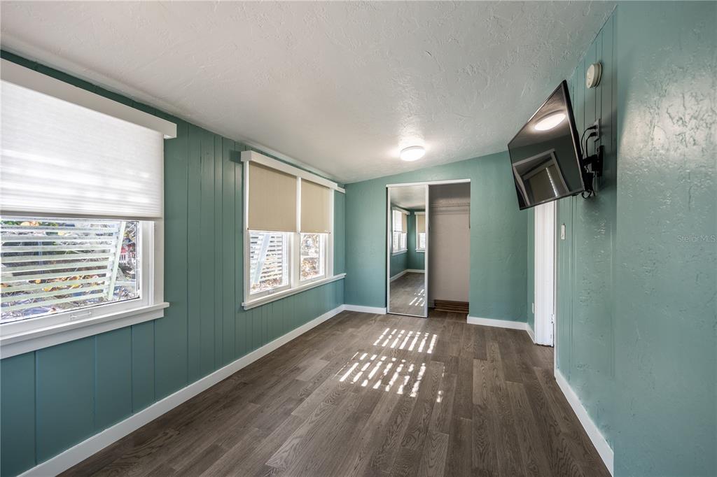 A room with teal paneled walls, wood-look flooring, a mirrored closet, and a wall-mounted television — 115 124TH AVENUE W, TREASURE ISLAND, FL