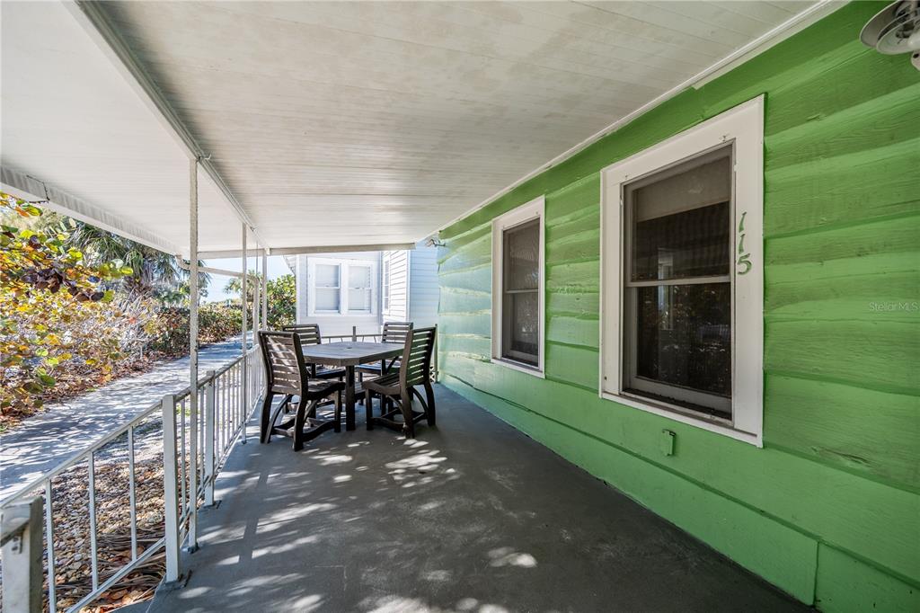 A covered porch with a concrete floor, green siding, and a small outdoor dining set — 115 124TH AVENUE W, TREASURE ISLAND, FL