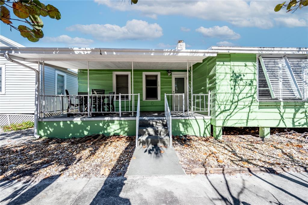 A light green house with a covered front porch, white railings, and a concrete walkway — 115 124TH AVENUE W, TREASURE ISLAND, FL