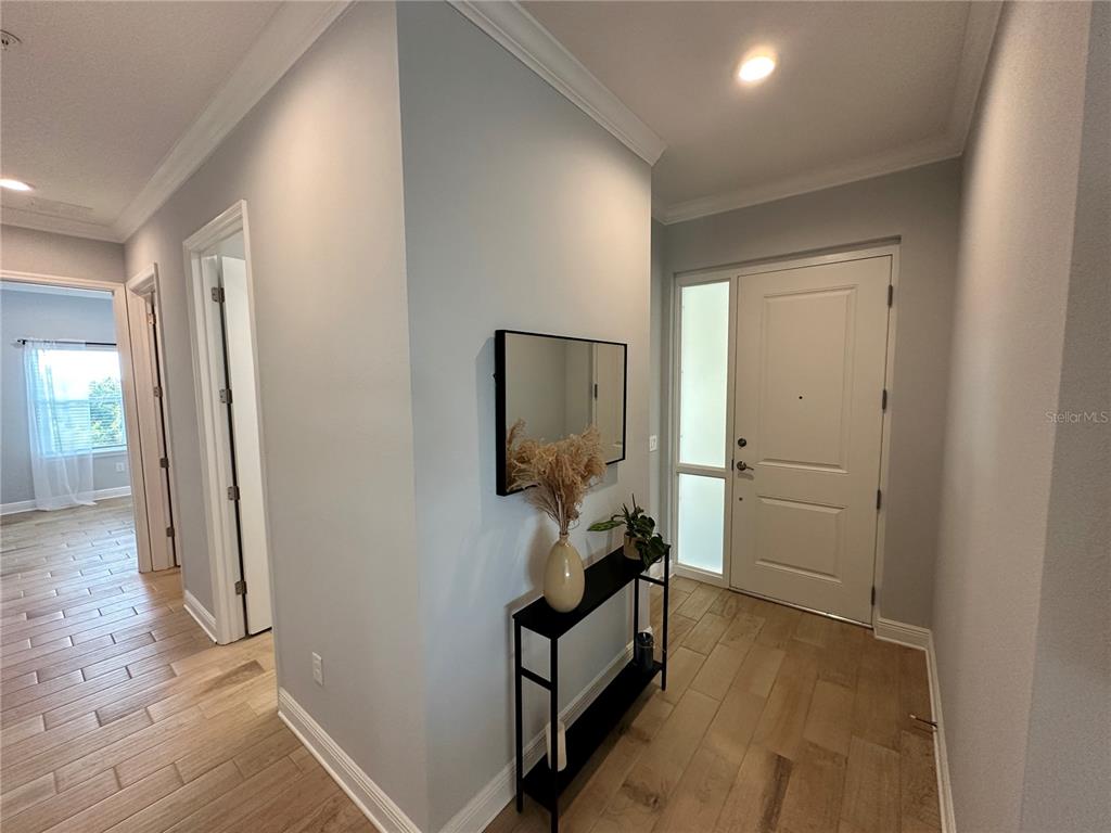 An entryway features light wood flooring, a black console table, a mirror, and a front door — 3426 W 79 STREET W UNIT 303, BRADENTON, FL