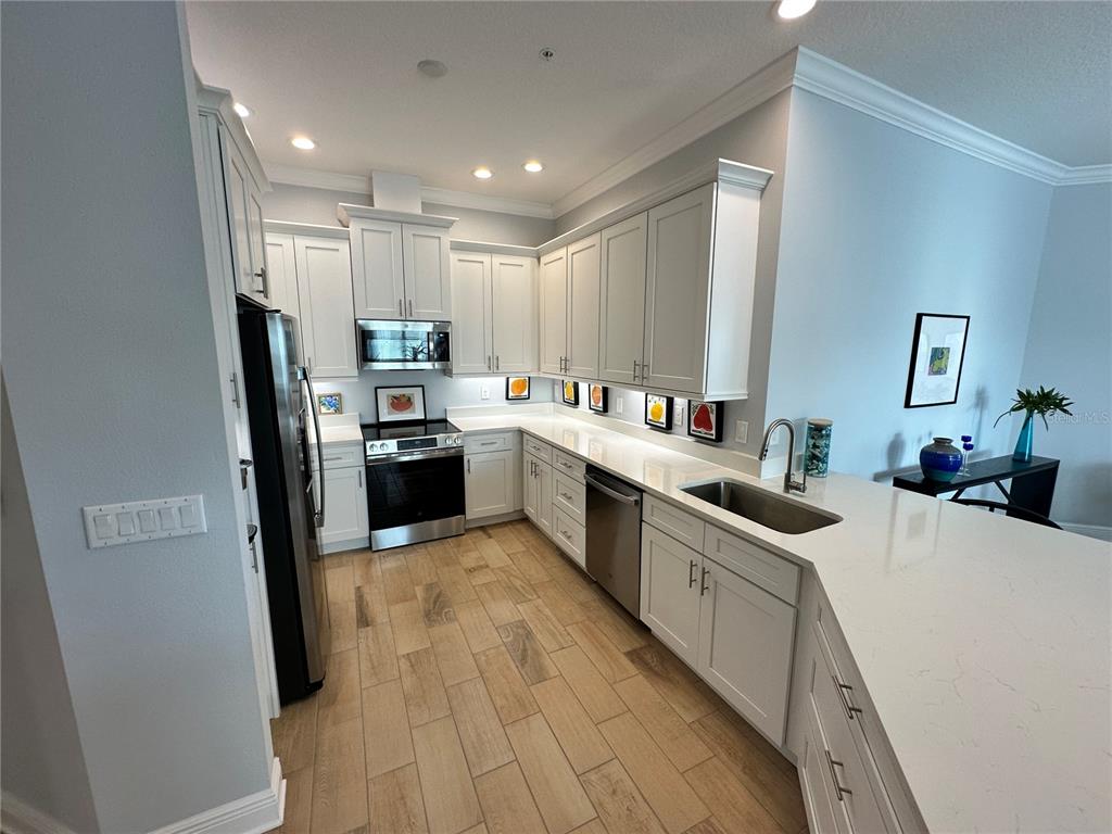 A modern kitchen features white cabinetry, stainless steel appliances, quartz countertops, and light wood-look flooring — 3426 W 79 STREET W UNIT 303, BRADENTON, FL