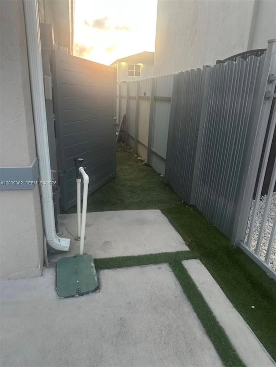A narrow side yard features artificial turf, a concrete path, and a gray privacy fence — HOMESTEAD, FL