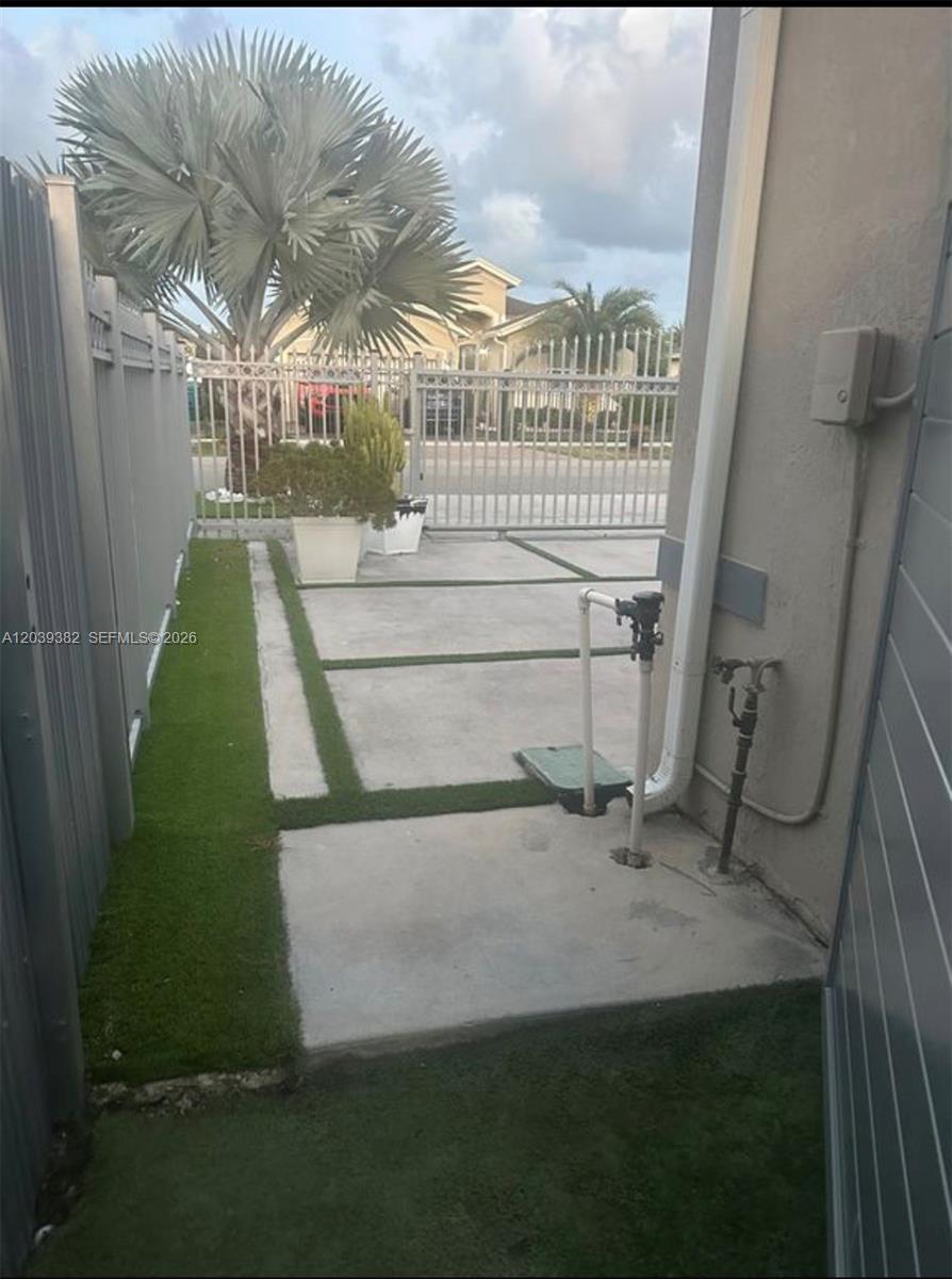 A concrete side yard features artificial turf strips, a metal fence, and utility pipes — HOMESTEAD, FL