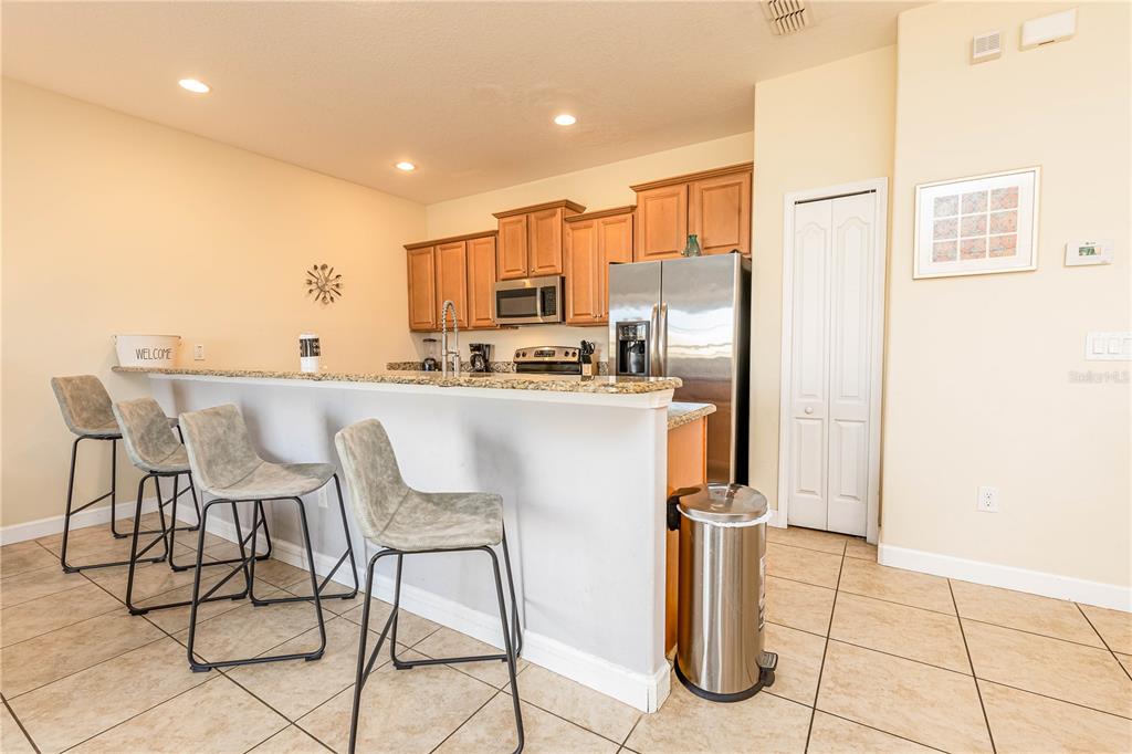 A kitchen features light wood cabinets, granite countertops, a breakfast bar, and stainless steel appliances — 8873 CANDY PALM ROAD, KISSIMMEE, FL