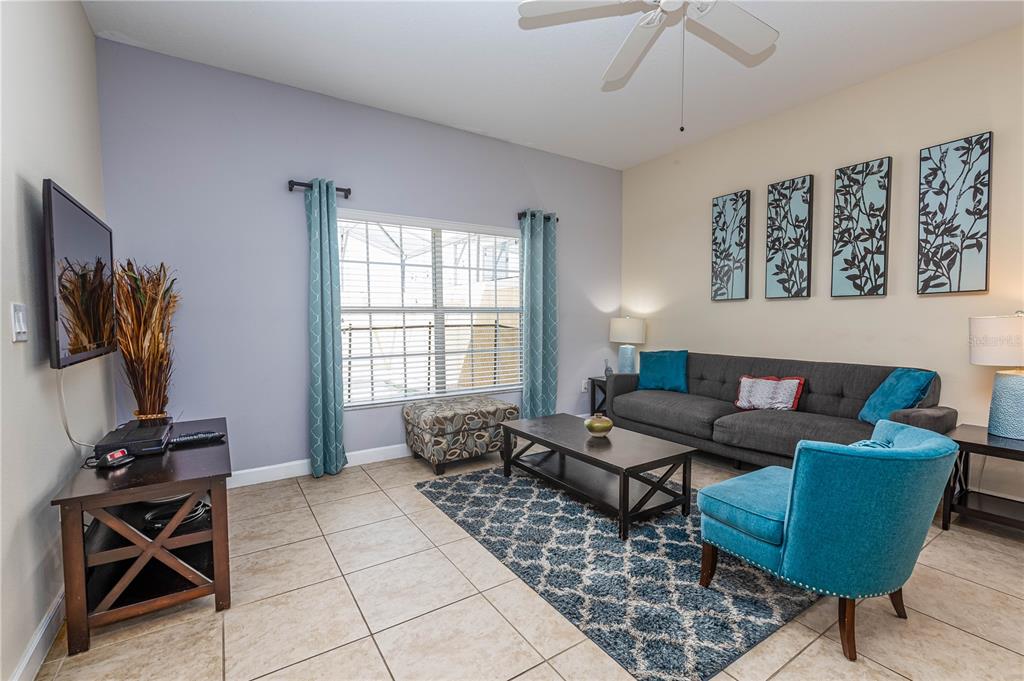 A living room features a gray sofa, a blue armchair, tile flooring, and a ceiling fan — 8873 CANDY PALM ROAD, KISSIMMEE, FL