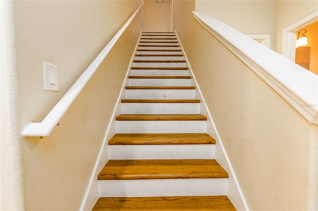 A straight wooden staircase with white risers leads upward between two beige walls — 8873 CANDY PALM ROAD, KISSIMMEE, FL